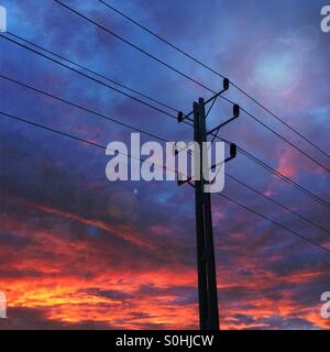 Strommasten und Kabel mit Abendsonne, im Hintergrund die schafft einen bunten Himmel hinunter Stockfoto