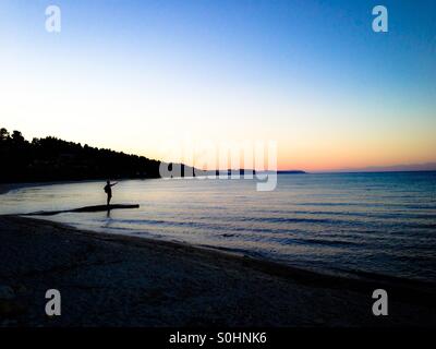 Mann am Steg Hinweisen zum Meer bei Sonnenuntergang über stilles Wasser Stockfoto