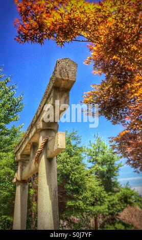 Japanische steinerne Torii Tor umrahmt von gold und rot japanischen Acer Bäume in einem Garten Stockfoto