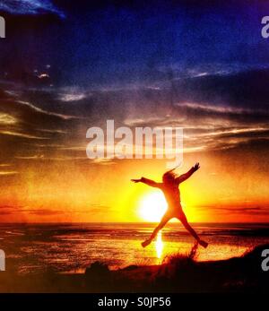 Springen Sie vor Freude gegen die untergehende Sonne über Morecambe Bay Stockfoto