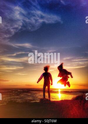 Zwei junge Mädchen, die Spaß vor der untergehenden Sonne zu springen