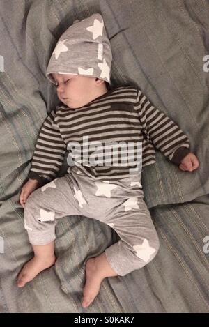 Baby Junge gekleidet in eine niedliche Sterne Hose und Hut zusammen mit abgestreift Pullover, friedlich schlafend auf einer Decke Stockfoto