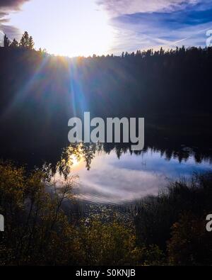 Sonnenuntergang über einem Hügel. Der kleine See fängt die Reflexion des umliegenden Waldes und die untergehende Sonne. Stockfoto