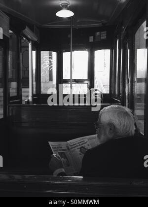 Mann, die Zeitung zu lesen, wie er auf die Standseilbahn Straßenbahn in Lissabon, Portugal wartet Stockfoto