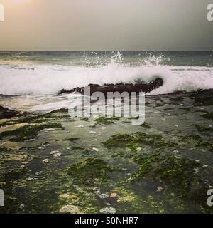 Wellen, die über Felsen bei Sonnenuntergang Stockfoto