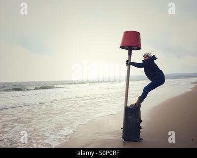 Frau mit Spaß balancieren auf Markierungsboje auf Dorset Strand im Winter Stockfoto