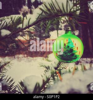 Grüne alte altmodische Christbaumkugel Darstellung einen Weihnachtsbaum hängt auf einem Ast im verschneiten Wald. Retro-bearbeiten. Stockfoto