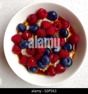 Schüssel Haferbrei mit Heidelbeeren und Himbeeren und Ahornsirup zum Frühstück Stockfoto