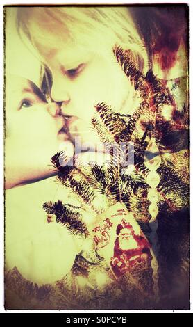 Schwestern küssen hinter den Weihnachtsbaum (Double Exposure) Stockfoto