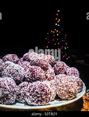 Ein Teller voller Kokos Rumkugeln vor einem Weihnachtsbaum. Stockfoto