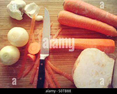 Verschiedene Gemüse (Zwiebel, Karotte, Sellerie) und ein Messer auf ein Schneidebrett für die Küche vorbereitet Stockfoto