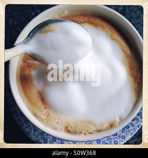 Schaumige Caffè Latte in blauen Tasse und Untertasse mit Löffel Stockfoto