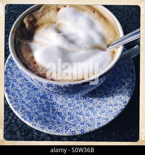 Blumige blaue Tasse und Untertasse mit schaumigen Cafe Latte und Löffel Stockfoto