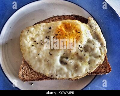 Gebratenes Ei auf Toast mit grob gemahlener schwarzer Pfeffer, präsentiert auf einem blau-weißen Teller