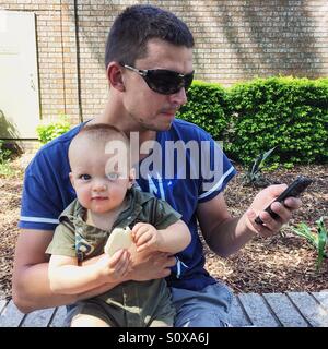 Vater Holding Baby und Blick auf Handy Stockfoto