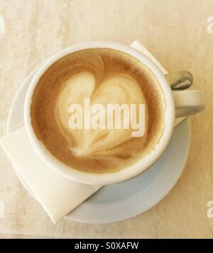 Kaffee mit herzförmigen Schaum in weißen Tasse und Untertasse auf Serviette mit Löffel Stockfoto