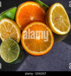 Orangen-Zitronen und Limetten in Scheiben geschnitten auf einer reflektierenden Oberfläche. Stockfoto