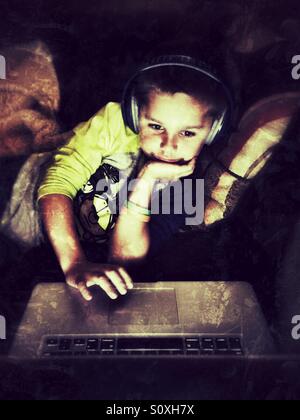 Kleiner Junge mit Kopfhörern verwendet einen laptop Stockfoto