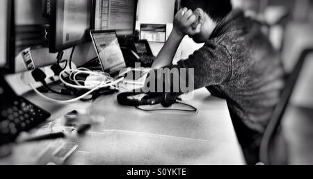 Ein Mann hängt seinen Kopf seine Hand, wie er auf einem Laptopcomputer an einem Schreibtisch in einem Büro arbeiten. Stockfoto