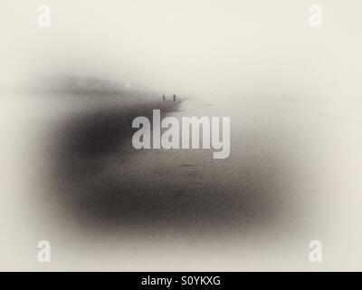 Menschen bei dichtem Nebel Wetter bei Sonnenaufgang am Strand entlang spazieren. Stockfoto