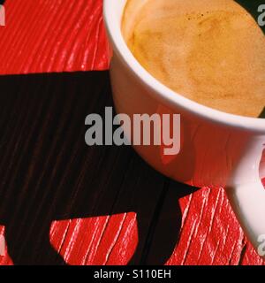 Ein overhead Nahaufnahme eines frischen Kaffee Americano Getränkes auf einem roten Holztisch. Eine einfache Komposition mit einem dunklen Schatten. Stockfoto