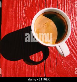 Ein overhead Nahaufnahme eines frischen Kaffee Americano Getränkes auf einem roten Holztisch. Eine einfache Komposition mit einem dunklen Schatten. Stockfoto