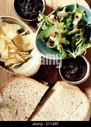 Käse-Sandwich serviert auf einem Holzbrett mit einem Beilagensalat, Chips und chutneys Stockfoto