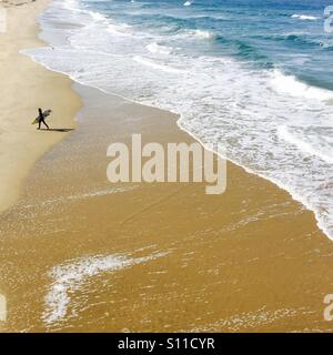 Eine einsame Surfer geht bis zum Strand.  Manhattan Beach, Kalifornien USA.
