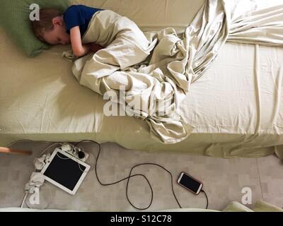 Junge mit iPad, Tablet und Smartphone, iPhone aufladen auf dem Boden schlafen Stockfoto