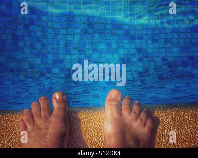 POV-Füße am Rande eines Swimmingpools Stockfoto