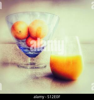 Drei Orangen in eine Glasschüssel mit einem Glas Orangensaft neben. Stockfoto