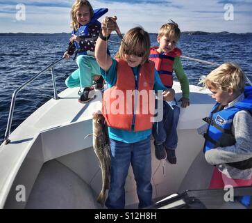 Drei Kinder zusehen, wie eine vierte einen frisch gefangenen Kabeljau Fisch hält. Stockfoto