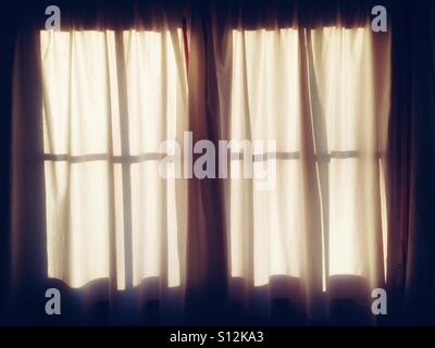 Ein Oberlicht-Fenster mit weißen Vorhängen im sanften Licht der Morgensonne Stockfoto