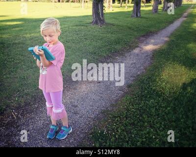 Ein junges Mädchen fängt Pokémon in einem lokalen Park. Stockfoto