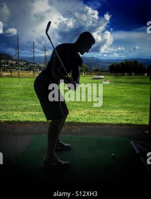 Silhouette eines jungen Mannes schlagen Golfbälle auf einer driving Range an einem sonnigen Tag im Freien. Stockfoto