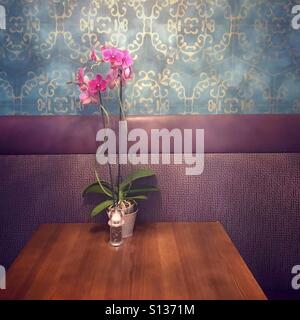Rosafarbene Orchidee auf einem Holztisch in einem luxuriösen Hotelrestaurant, fotografiert in sanfter, stilisierter, atmosphärischer Stimmung. Stockfoto