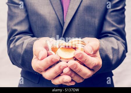 Ein Geschäftsmann im Anzug mit einer Handvoll von Gold- und Silbermünzen in den hohlen Händen. Stockfoto