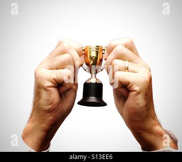 Ein paar Hände halten eine kleine Trophäe in der Feier des Gewinnens und auf einem weißen Hintergrund. Stockfoto