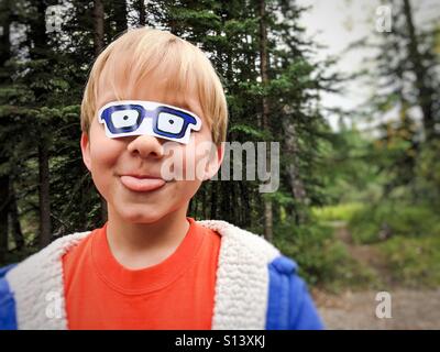 Ein Junge ragt seine Zunge, wie er mit einem Aufkleber ähnlich Brille stecken über seine Augen spielt. Stockfoto