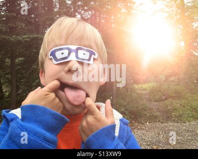 Ein Junge steckt seine Zunge machen ein lustiges Gesicht, spielen im Freien. Stockfoto