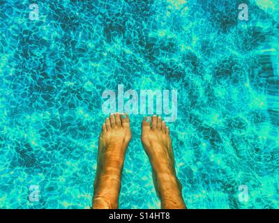 Füße im Pool, Sonne auf dem Wasser reflektiert. Stockfoto