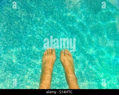 Frau die Füße baumeln im blauen Wasser des Pools an einem sonnigen Tag. Stockfoto