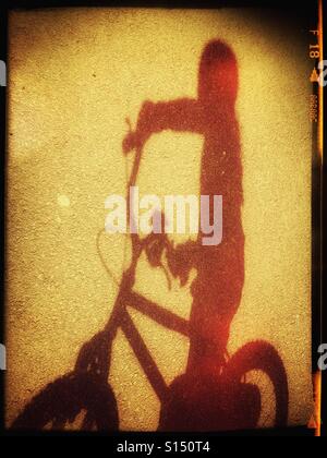 Einem roten Schatten eines Kindes mit dem kleinen Fahrrad. Der Schatten ist auf einer Fläche von Asphalt (Asphalt). Bildnachweis - © COLIN HOSKINS. Stockfoto