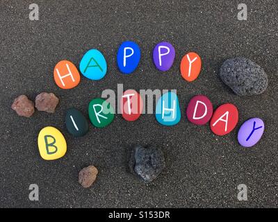 Happy Birthay Text, komponiert mit mehrfarbigen Steinbuchstaben über natürlichem schwarzem Sand von Vulcano Island, Äolischen Inseln, Sizilien, Italien Stockfoto