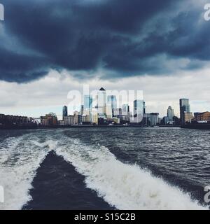 Skyline von London Docklands von einem Boot auf der Themse mit stürmischen Wolken gesehen. Stockfoto