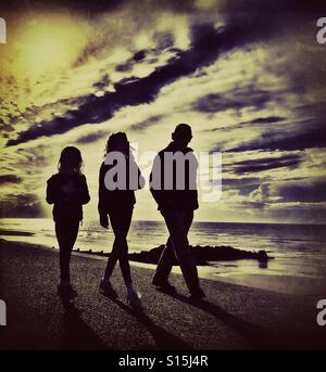 Drei Menschen in Silhouette entlang am Meer (Erwachsene und zwei Kinder) Stockfoto