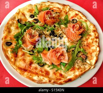 Pizza mit Räucherlachs, Rucola und schwarzen Oliven Stockfoto