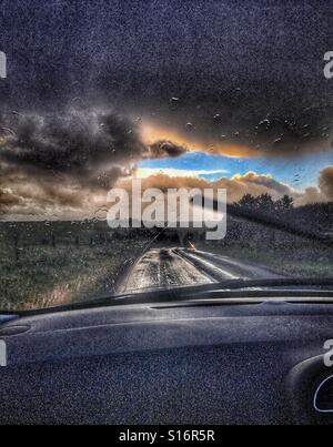 Auf der Suche durch Auto Windschutzscheibe, Landstraße, entgegenkommenden Scheinwerfern und stürmischen Himmel Stockfoto