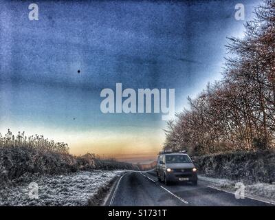 Auf der Straße im Winter. Am frühen Morgen mit sehr starkem Frost. Entgegenkommendes Fahrzeug mit Scheinwerfer auf. Stockfoto