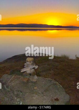 Inuksuk Denkmal auf dem Felsvorsprung am See mit Sonne über Forest Hills Stockfoto